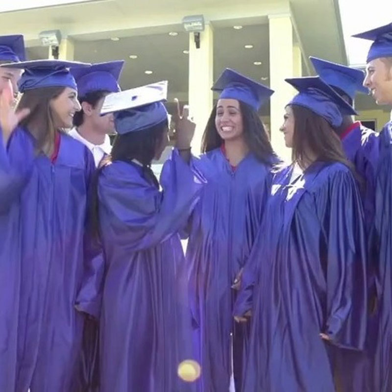 Smiling graduates in blue caps and gowns gather outdoors